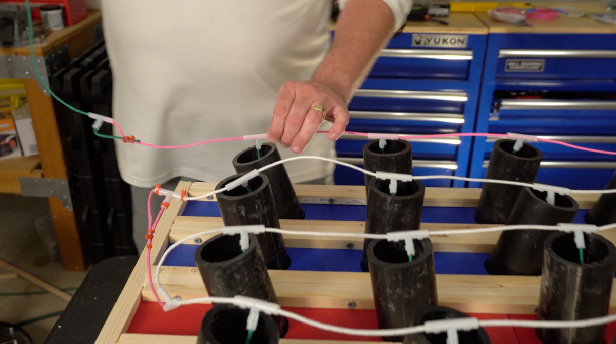 Overhead view of hands stringing quick-match fuse between mortar tubes on the finished rack