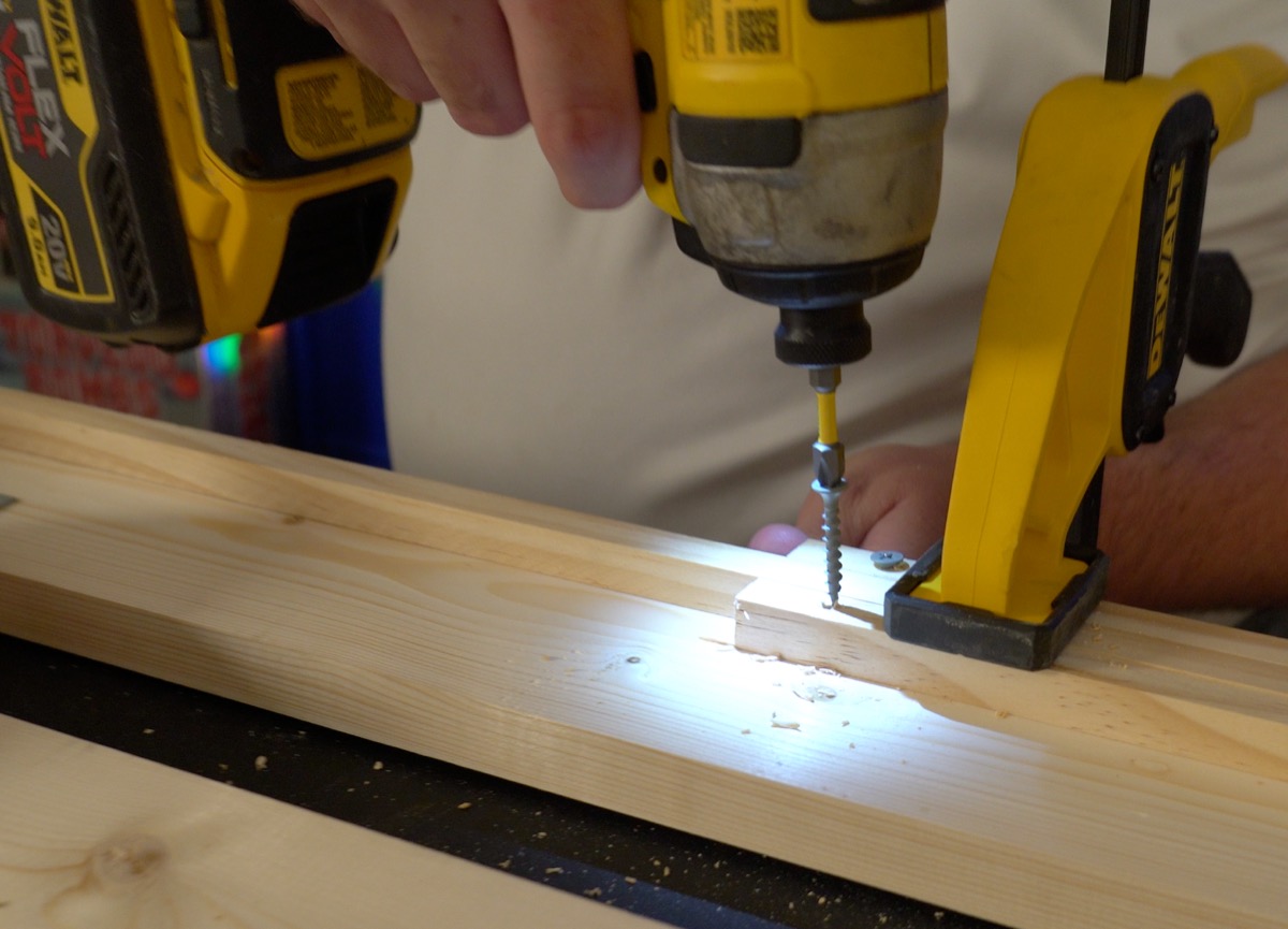 DeWalt impact driver sinking a screw through a wood block into a pine rail