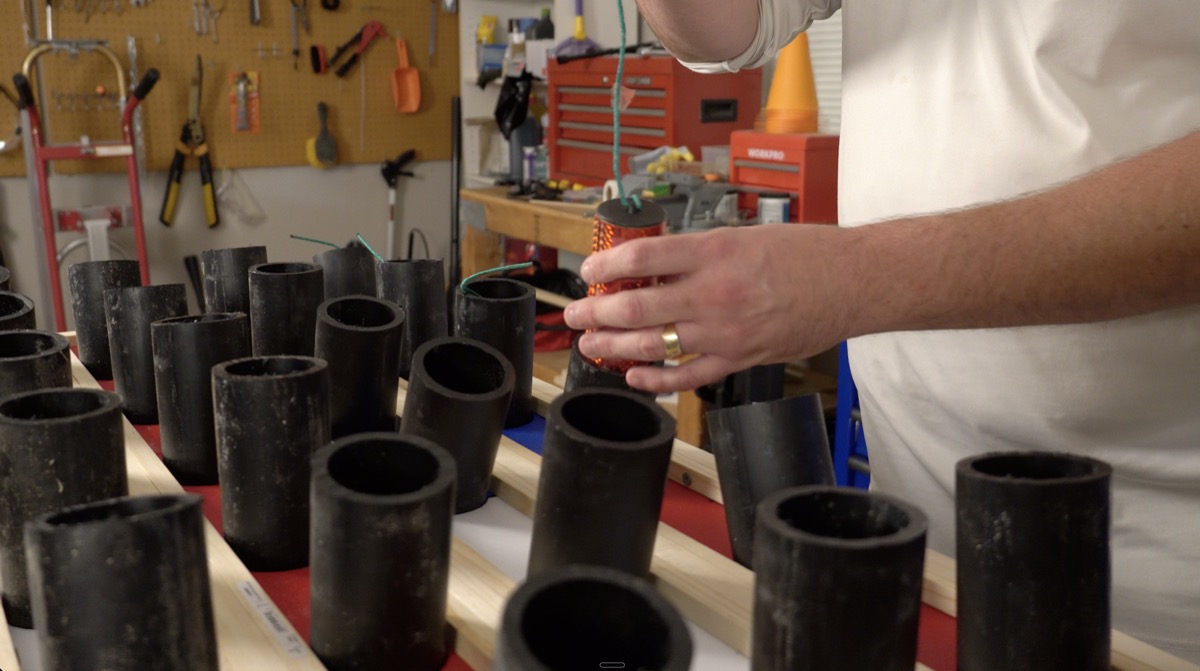 Lowering an orange foil-wrapped shell toward a mortar tube