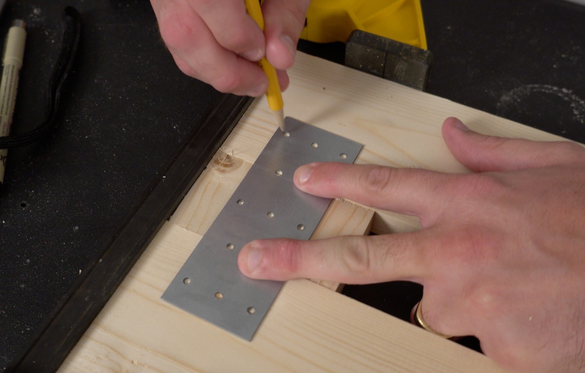 Marking pilot holes through a Simpson Strong-Tie plate with a yellow pencil